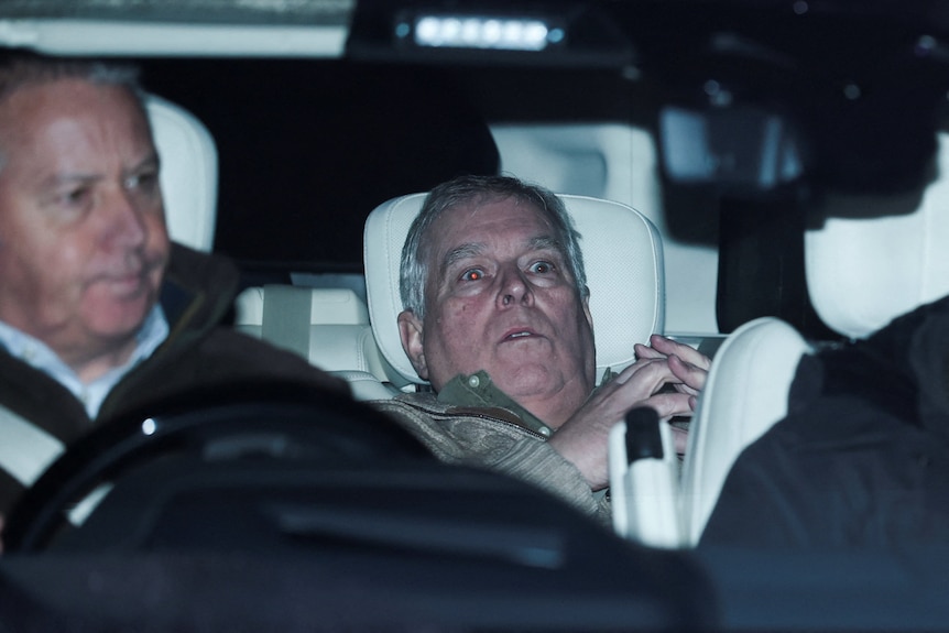 Andrew Mountbatten-Windsor lies down with wide eyes in a car, a man in front of him.