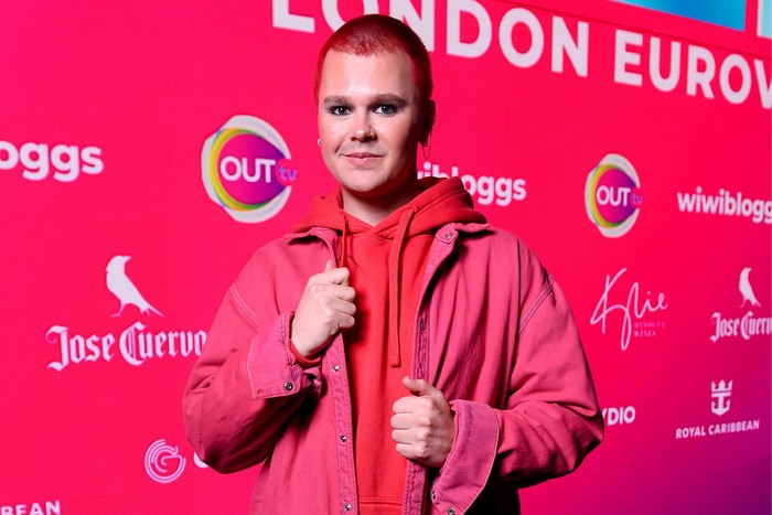 A person dressed in all red, smiling ahead while holding onto the lapels of their jacket.