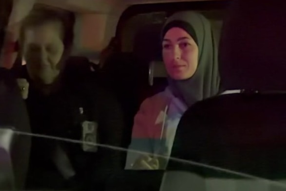 A woman in a hijab sits next to a man in the back of a car at night.