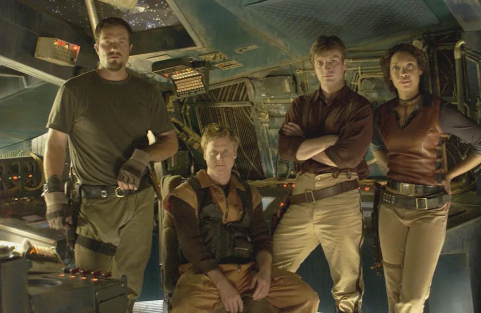 Four actors in sci-fi costumes stand inside a spaceship set. They are in a relaxed, confident pose, reflecting a space adventure theme