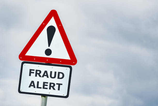 Warning road sign with exclamation mark above a “Fraud Alert” sign against a cloudy sky.