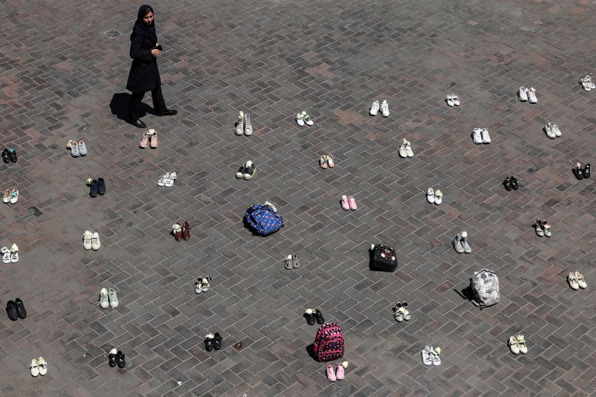 A woman walks past symbolic belongings laid on the ground at Valiasr Square in Tehran on April 24, 2026, in tribute to the schoolgirls in Minab killed during the initial February 28 airstrikes on Iran.