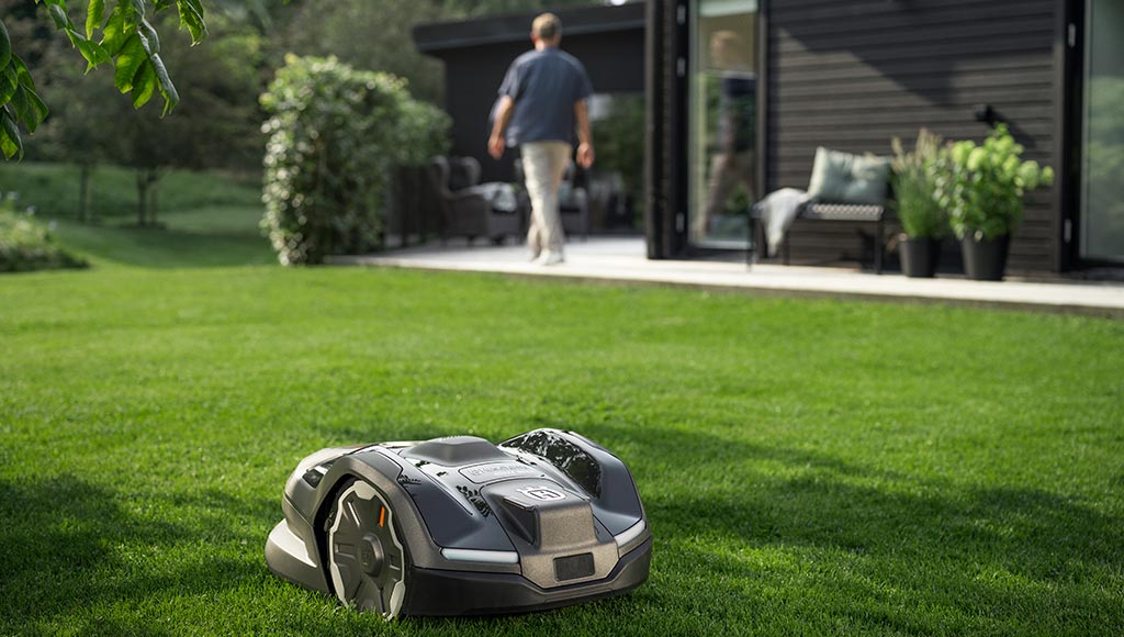 A yard with lots of green space and the lawn being mowed by a Husqvarna lawnmower