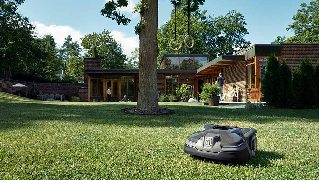A Husqvarna lawnmower working on a large green space in front of a house 