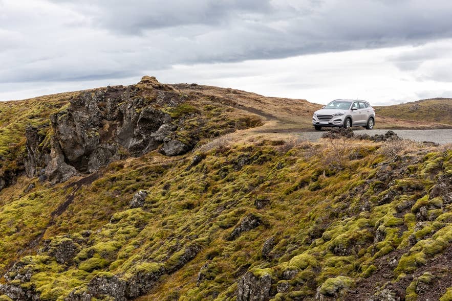 Car parked on a mossy lava hill during a scenic spring drive, showing rugged landscapes in Iceland in April. Car parked on a mossy lava hill during a scenic spring drive, showing rugged landscapes in Iceland in April.
