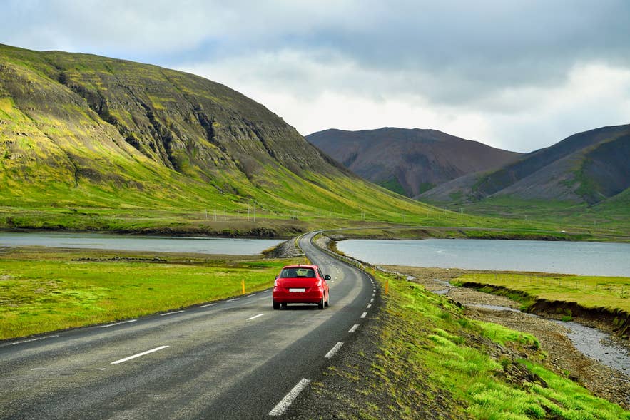 Red car driving through green fjord landscapes, capturing a scenic spring road trip in Iceland in April. Red car driving through green fjord landscapes, capturing a scenic spring road trip in Iceland in April.