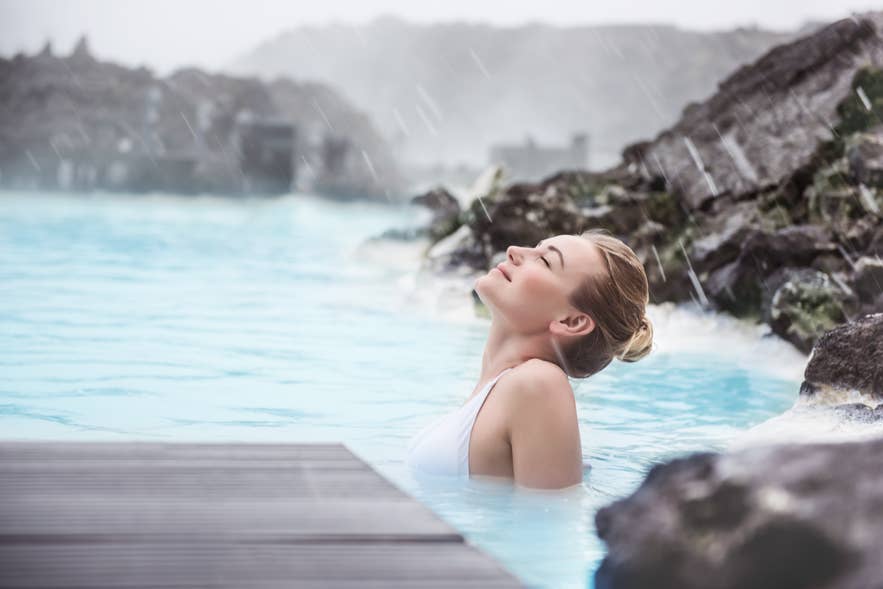 Woman relaxing in the warm Blue Lagoon during light rain, showing the geothermal experience in Iceland in April. Woman relaxing in the warm Blue Lagoon during light rain, showing the geothermal experience in Iceland in April.