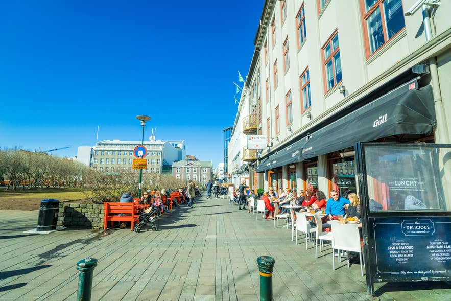 People dining outdoors on a sunny street in Reykjavik, showing what Iceland in April looks like in the city center. People dining outdoors on a sunny street in Reykjavik, showing what Iceland in April looks like in the city center.