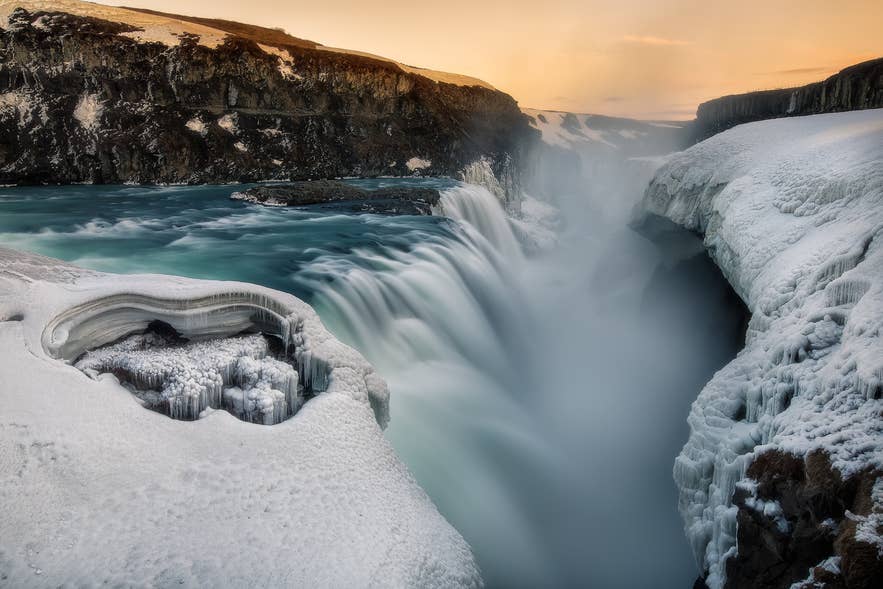 Gullfoss waterfall in winter Iceland with icy canyon cliffs and powerful cascading water at sunset.