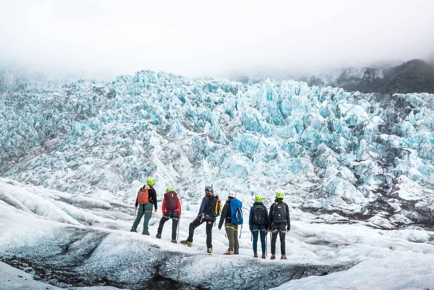 Group of hikers on an Iceland glacier hike, wearing helmets and crampons with a blue ice glacier backdrop.