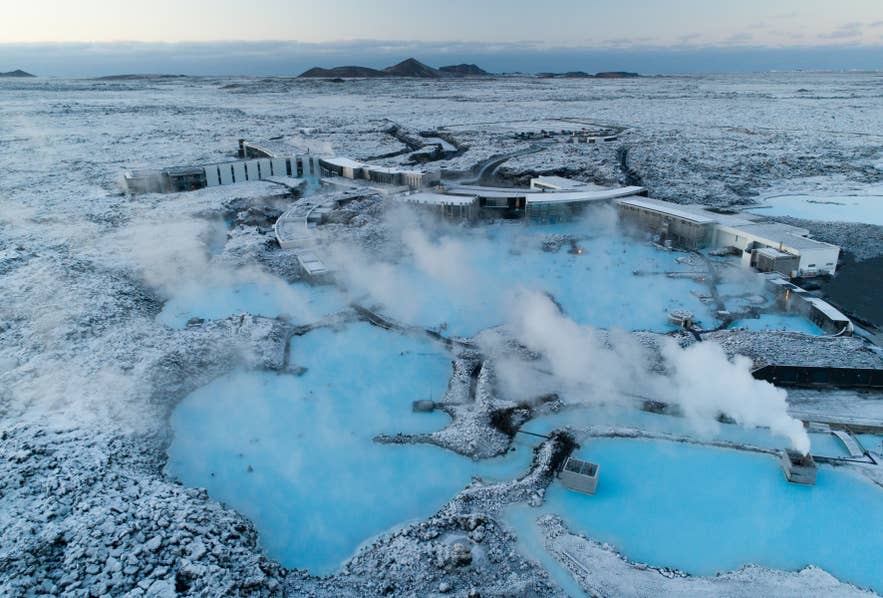 Aerial view of the Blue Lagoon geothermal spa in winter, Iceland, with steaming milky-blue pools surrounded by snowy lava fields.