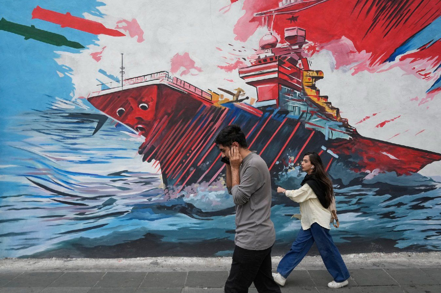 People walk past a mural depicting a U.S. aircraft carrier under missile attack in downtown Tehran.