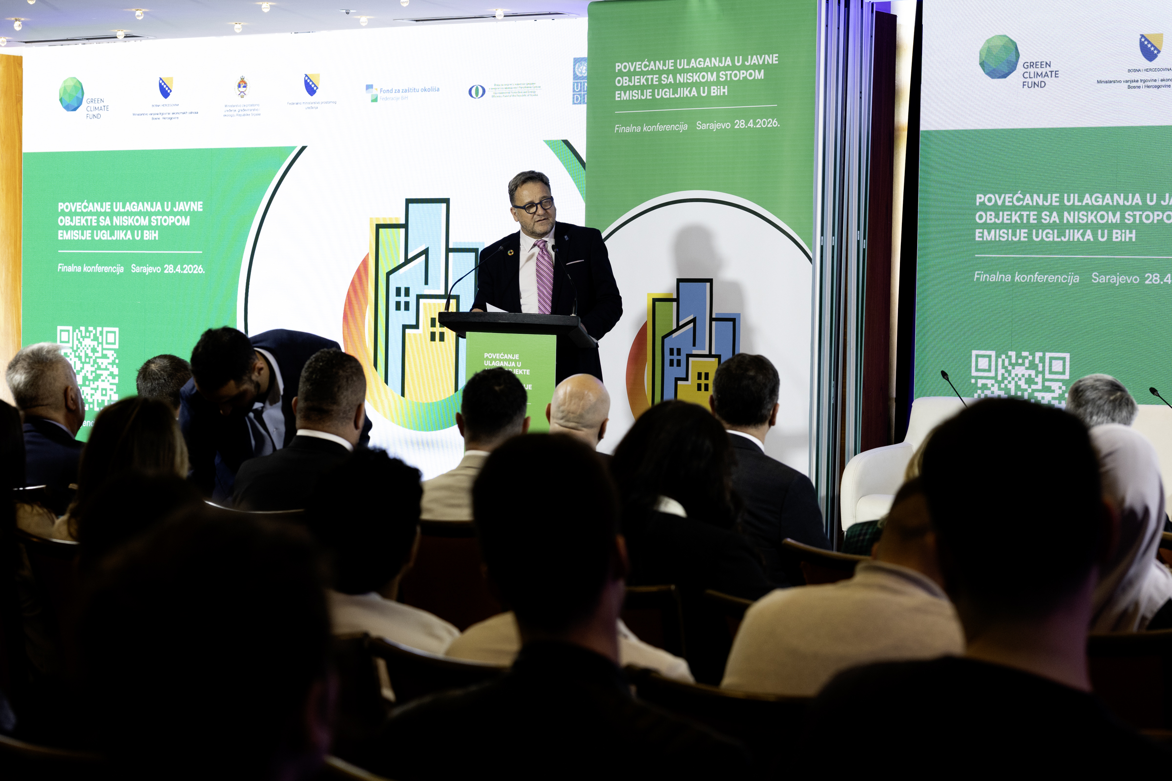 Photograph of a man at a podium delivering a talk at a conference with green banners.
