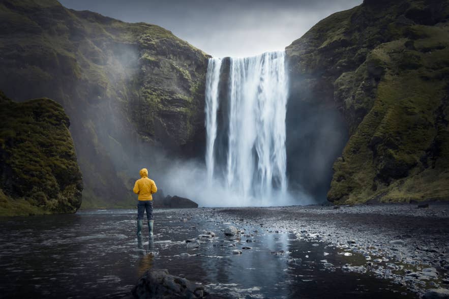 Traveler standing at Skogafoss Waterfall in South Iceland surrounded by mist and cliffs. Traveler standing at Skogafoss Waterfall in South Iceland surrounded by mist and cliffs.