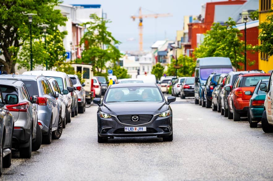 Car driving down a colorful Reykjavik street lined with parked cars and Icelandic houses Car driving down a colorful Reykjavik street lined with parked cars and Icelandic houses