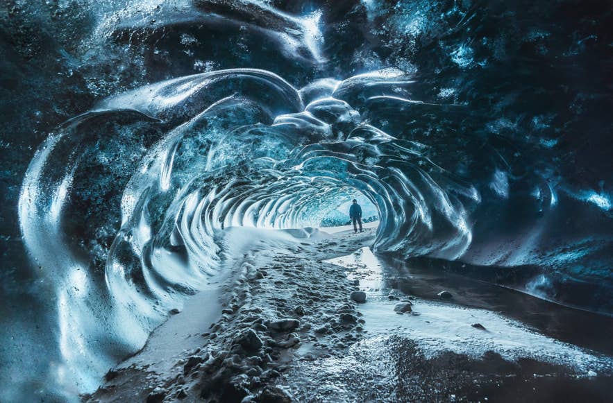 Person exploring inside a shimmering blue ice cave in Iceland with snowy floor and textured frozen walls Person exploring inside a shimmering blue ice cave in Iceland with snowy floor and textured frozen walls