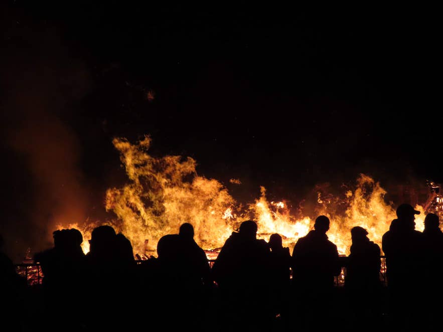 Silhouettes of people watching a large bonfire blaze against the night sky in Iceland Silhouettes of people watching a large bonfire blaze against the night sky in Iceland