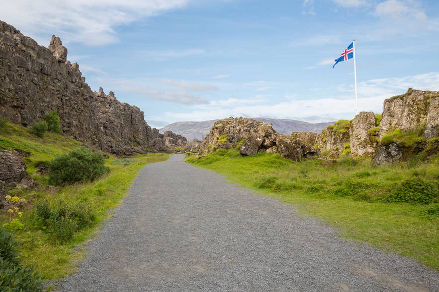 Path through Almannagja rift canyon at Thingvellir National Park with the Icelandic flag flying above the cliff Path through Almannagja rift canyon at Thingvellir National Park with the Icelandic flag flying above the cliff