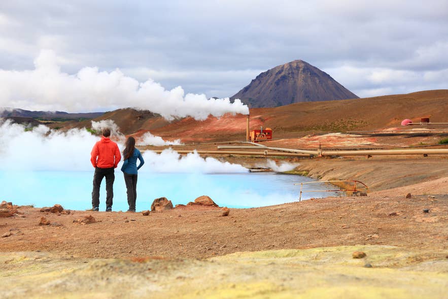 Two travelers viewing a steaming geothermal pool at Namafjall geothermal area near Lake Myvatn in north Iceland Two travelers viewing a steaming geothermal pool at Namafjall geothermal area near Lake Myvatn in north Iceland