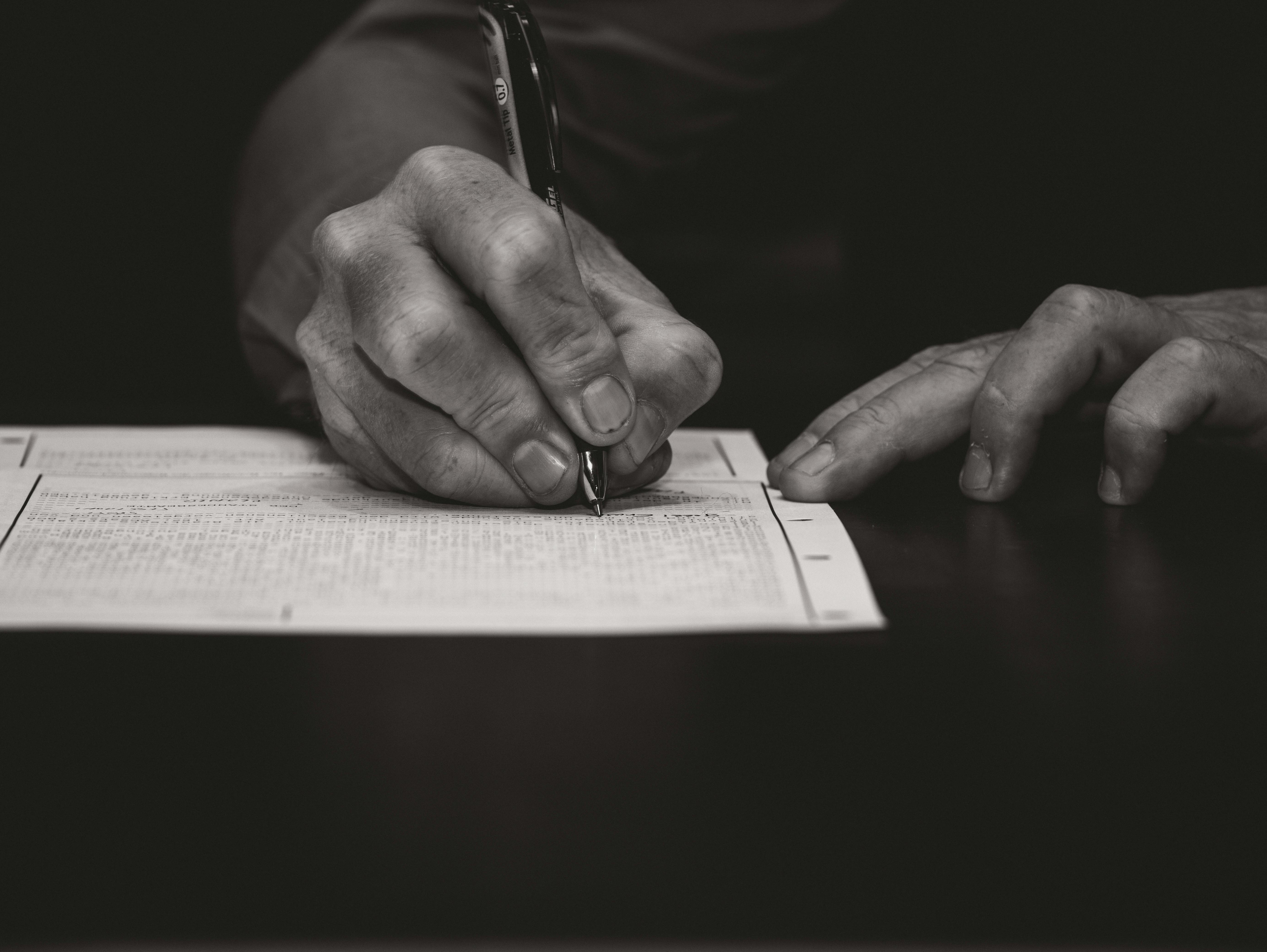 Close-up of a person filling out a printed form with a pen on a dark table