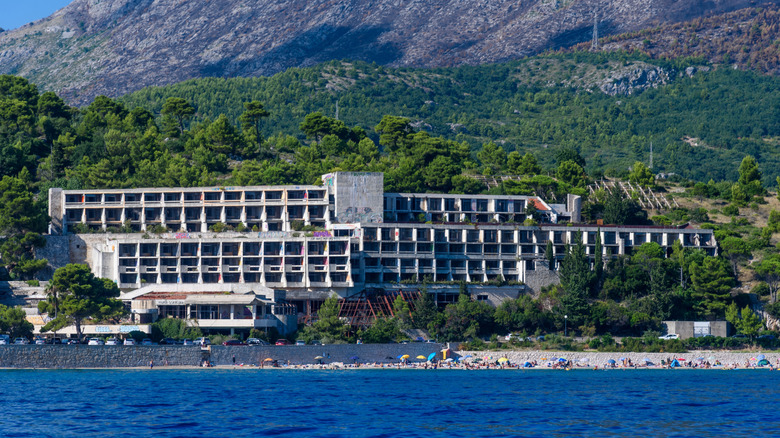 A large abandoned hotel surrounded by greenery at the base of a mountain