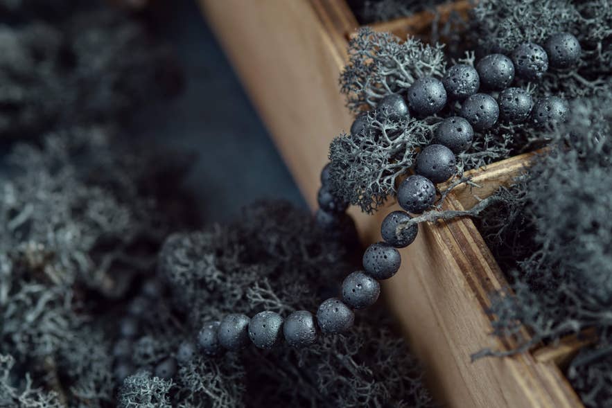 Black lava stone bead necklace resting on dried moss inside a wooden display box, showcasing Icelandic volcanic jewelry. Black lava stone bead necklace resting on dried moss inside a wooden display box, showcasing Icelandic volcanic jewelry.