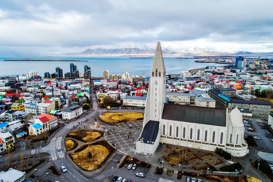 Aerial view of Hallgrimskirkja Church in Reykjavik with colorful buildings and snowy mountains in the background. Aerial view of Hallgrimskirkja Church in Reykjavik with colorful buildings and snowy mountains in the background.