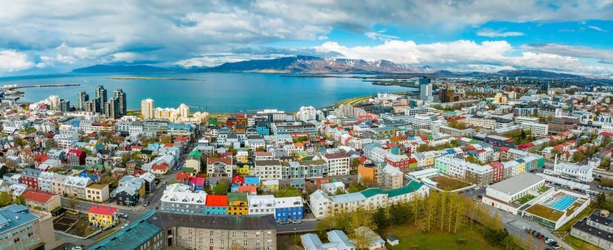 Aerial view of Reykjavik, showing colorful buildings, coastline, and distant mountains under a partly cloudy sky. Aerial view of Reykjavik, showing colorful buildings, coastline, and distant mountains under a partly cloudy sky.