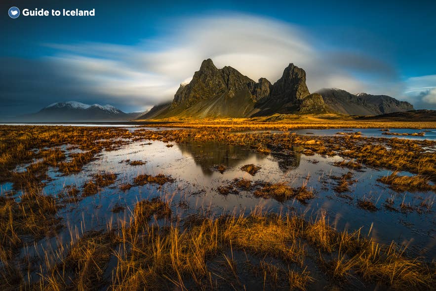 Scenic view of Vestrahorn mountain in Iceland with golden marshlands and reflections under dramatic skies at sunset.