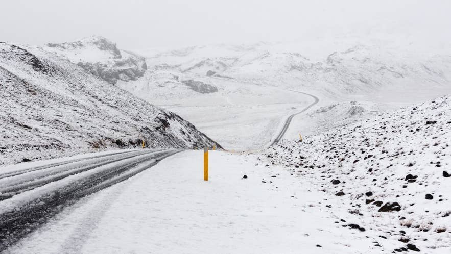 Snow-covered winding road through Icelandic mountains on a foggy winter day.