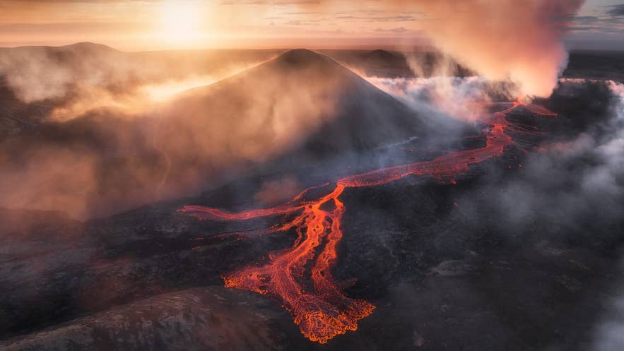 Molten lava flows from the Litli-Hrutur in Iceland, glowing under the smoky sky at sunset.