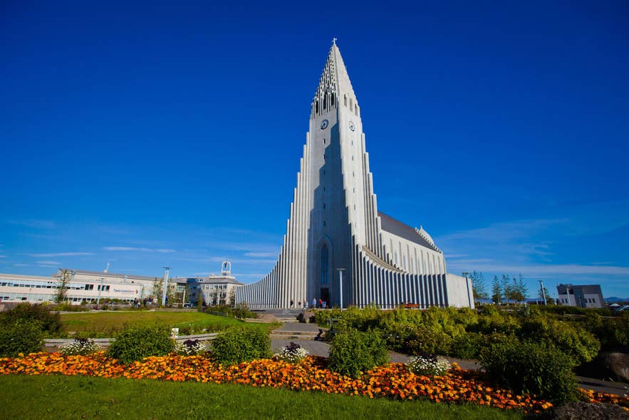 Hallgrímskirkja Church in Reykjavík, Iceland, on a clear summer day with bright blue sky, blooming orange flowers, and green landscaping