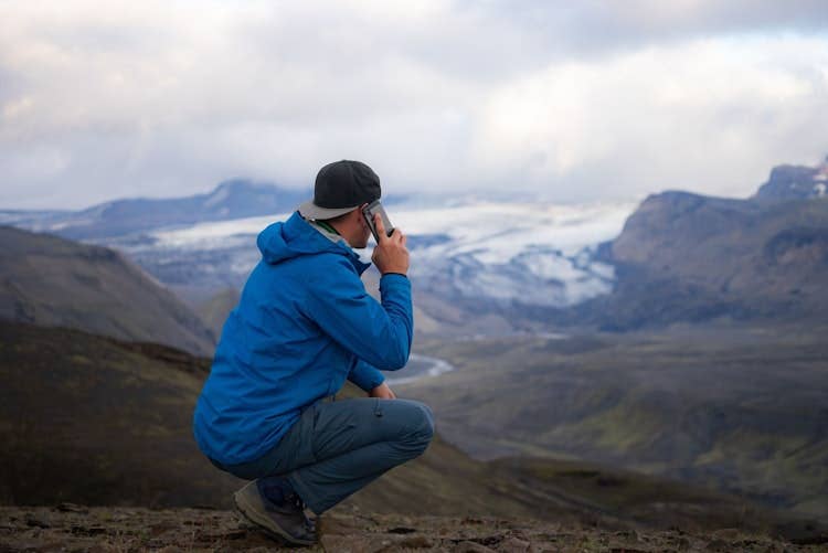 Traveler using phone on a mountain hike in Iceland, using an Iceland app for navigation, safety updates, and trip planning.