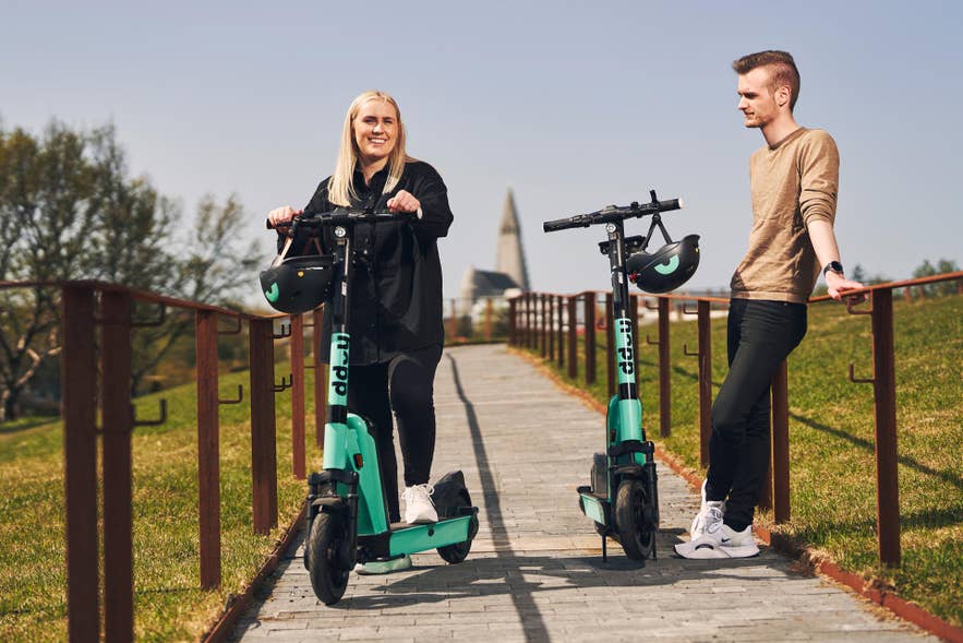 Two people with electric scooters in Reykjavik, enjoying city transport options often booked with an Iceland app like Hopp.