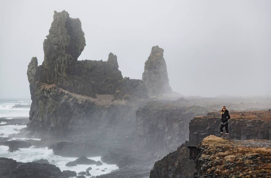 Traveler stands on cliffs at Londrangar in misty weather, a reminder to check forecasts with an Iceland app like Vedur.