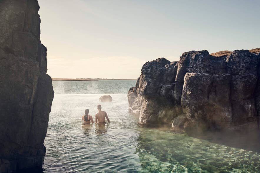 A couple entering Sky Lagoon, a natural hot spring lagoon between rocky cliffs in Reykjavik.