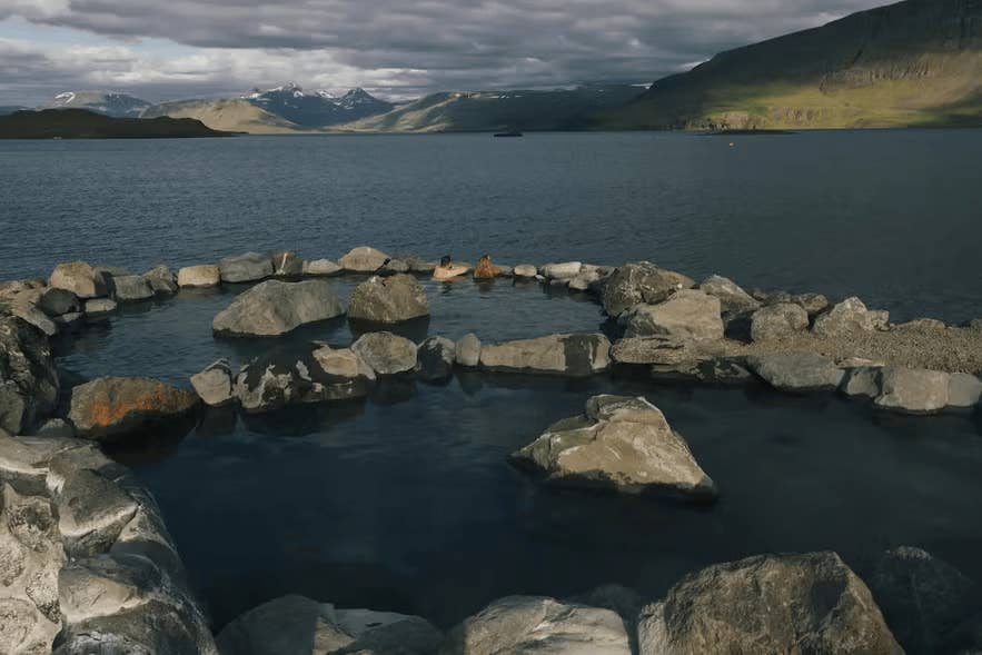 Hvammsvik Hot Springs, a stone-built hot spring pool beside a fjord with a mountain backdrop in Iceland.