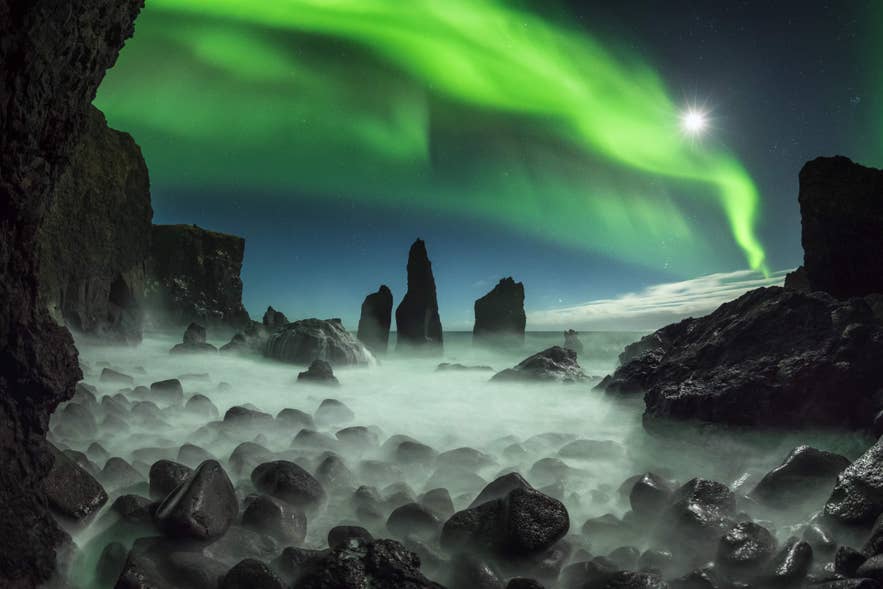 Northern lights in Iceland over a volcanic rock beach with sea mist.
