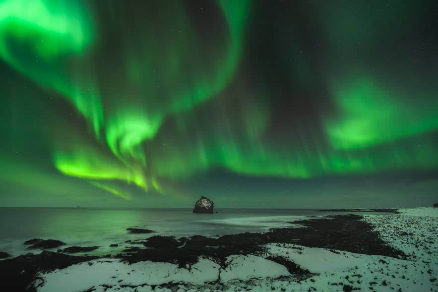 Northern lights over the sea in winter in Iceland with shimmering aurora borealis above the coastline.