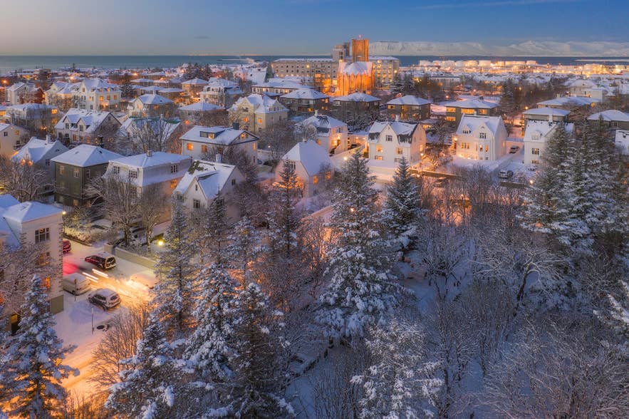 Snow-covered residential neighborhood in Reykjavik with glowing lights at dusk.