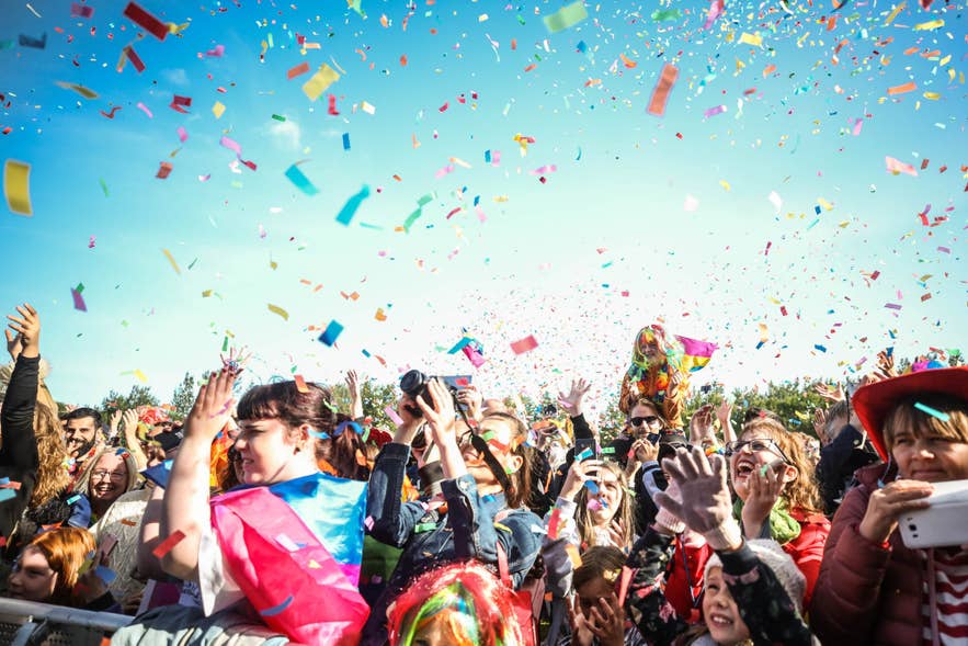 A crowd celebrating outdoors with rainbow confetti in the air at the Reykjavik Pride Festival.