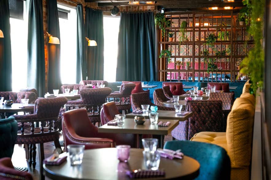 Colorful Fjallkonan Restaurant interior with upholstered chairs, floral wallpaper and Icelandic dining setting.
