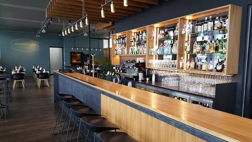 Modern cocktail bar interior with wooden counter, liquor display shelves, and stylish seating at Jörgensen Kitchen & Bar in Reykjavik.