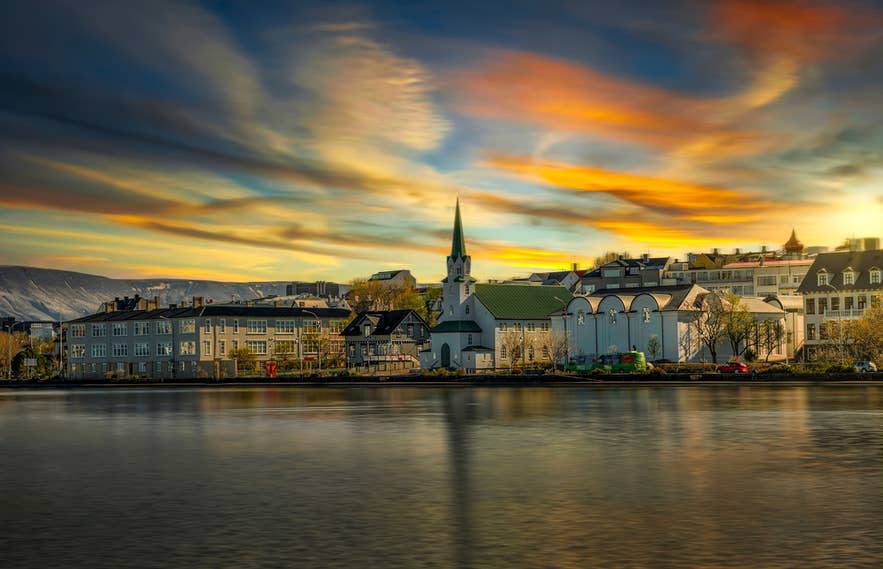 Colorful sunset over lakeside buildings and a church in the city center of Reykjavik.