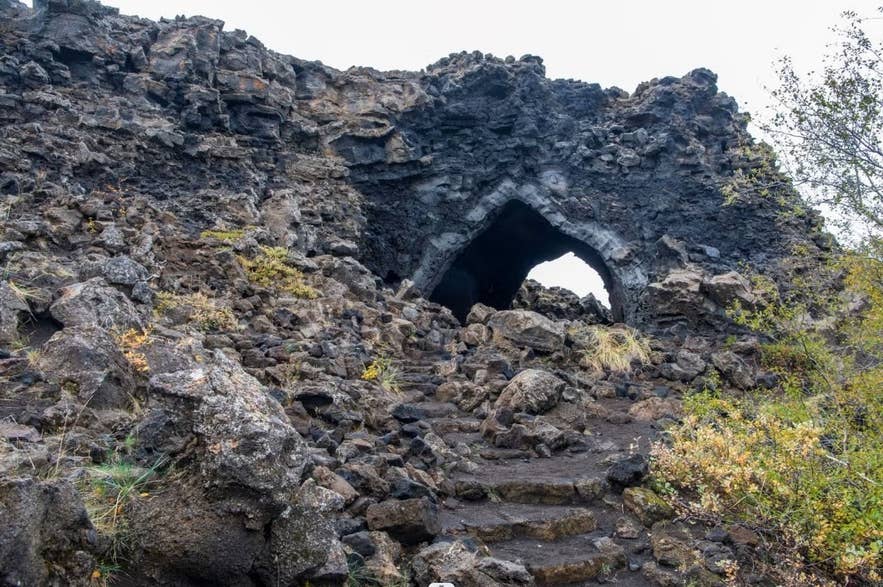 A lava rock archway at Dimmuborgir with a rocky path and some plants around it. A lava rock archway at Dimmuborgir with a rocky path and some plants around it.