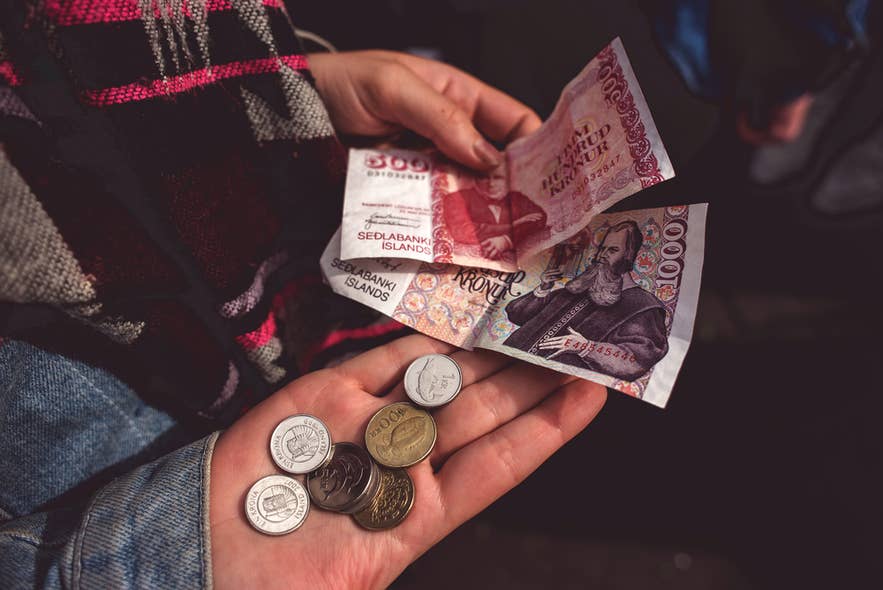 A person holding Icelandic banknotes and coins in both hands