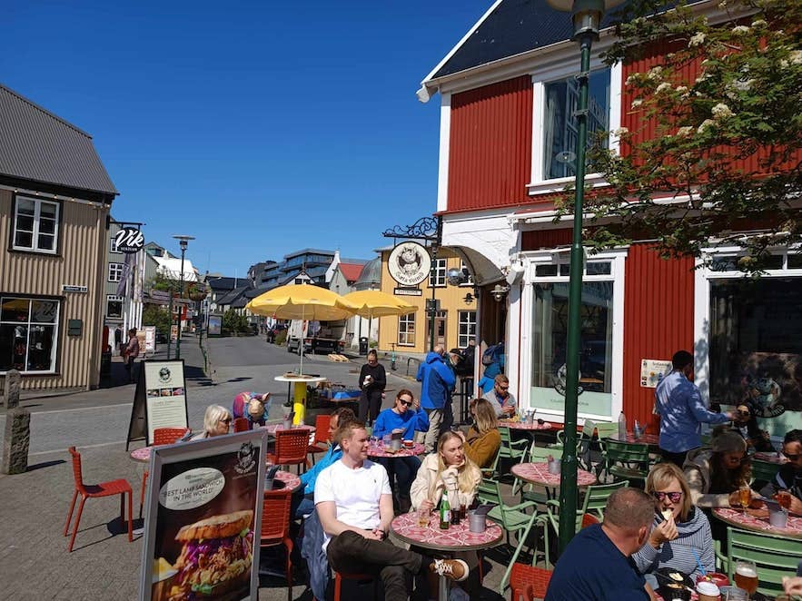 People dining at outdoor café tables along a sunny street in Reykjavik on a clear summer day.