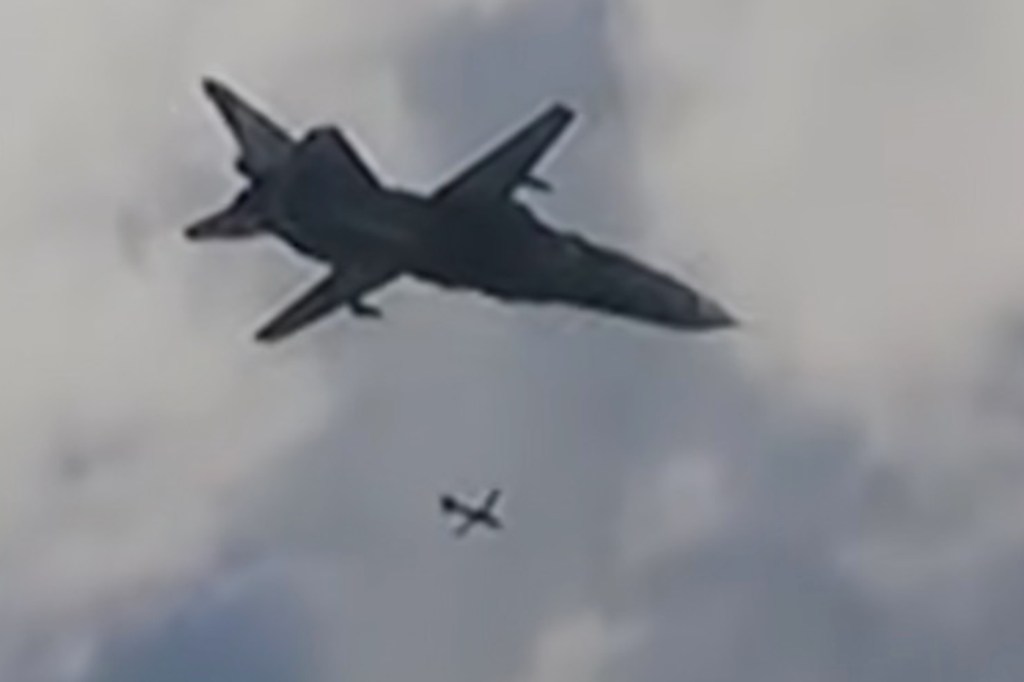A large jet aircraft releasing a smaller glide bomb against a cloudy sky.