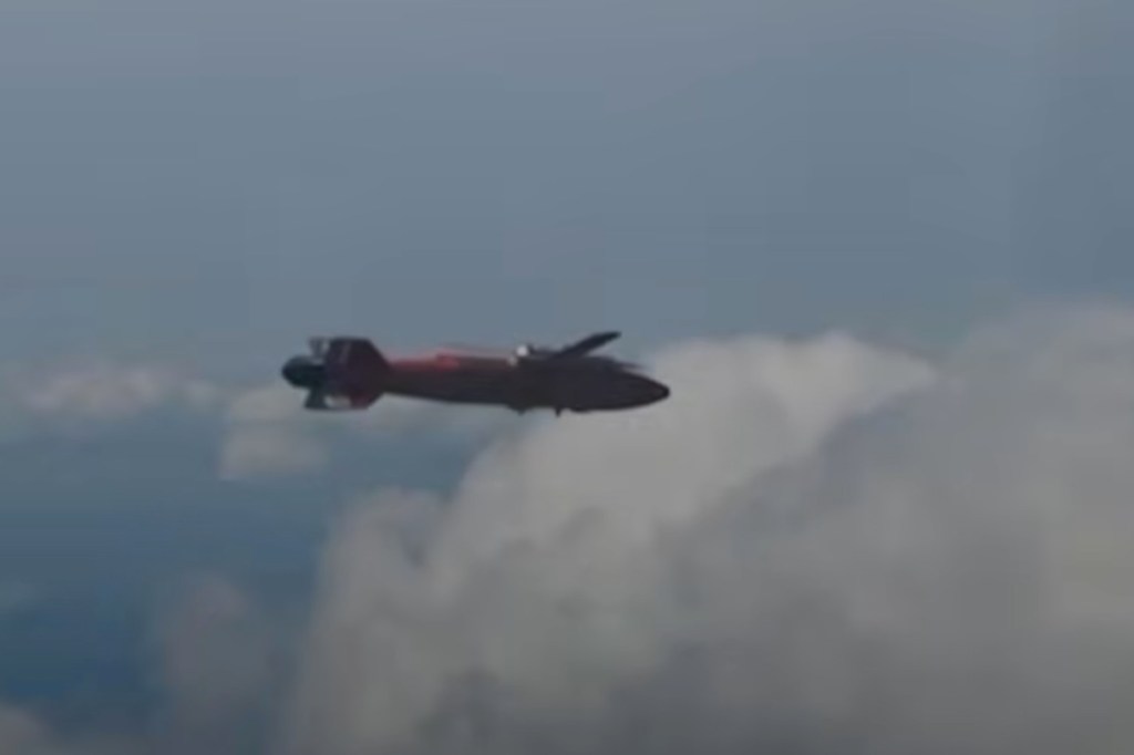A red glide bomb flying through the sky with clouds in the background.