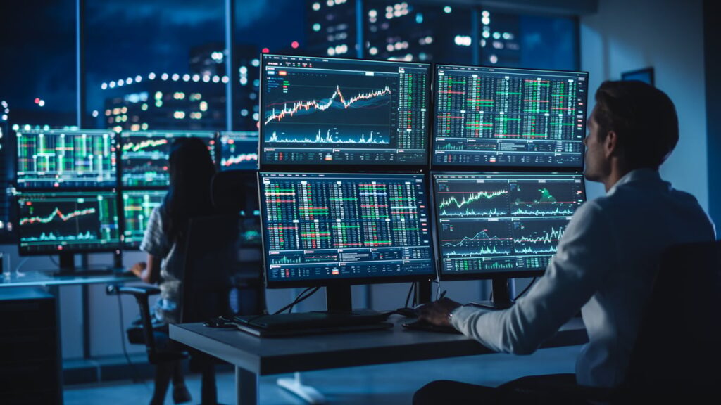 People looking at charts on computers in darkened office.